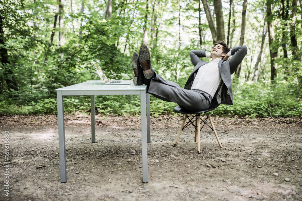 Great job. Relaxed business man in suit with heads over head and legs on office desk after successful work in green park. Freelancer relax after great deal in green forest. Business concept. Great job. Relaxed business man in suit with heads over head and legs on office desk after successful work in green park. Freelancer relax after great deal in green forest. Business concept.