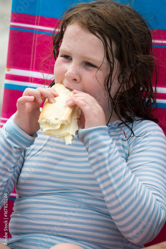 Child girl with cheese hoagie sandwhich on a deck chair by the ocean photo