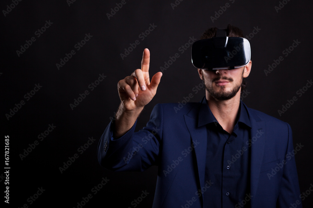 Businessman in suit with a VR headset on head touching a virtual button in studio photo on black background. Virtual reality and gestures Businessman in suit with a VR headset on head touching a virtual button in studio photo on black background. Virtual reality and gestures