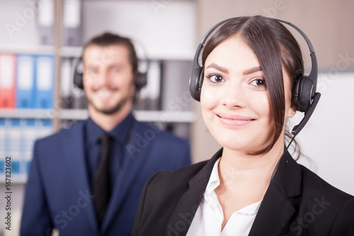 Woman working at the customer support and her colleague blurred in background. Help desk and support