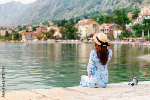 Девушка в шляпе смотрит вдаль, сидя на берегу моря (залива), Котор, Черногория