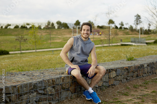 Happy Male Athlete Sitting On Gabion Wall photo