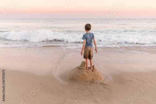 Boys standing on sandcastle waiting for the sea to destroy it