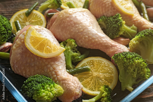 Fresh chicken legs with lemon and broccoli in baking dish, closeup