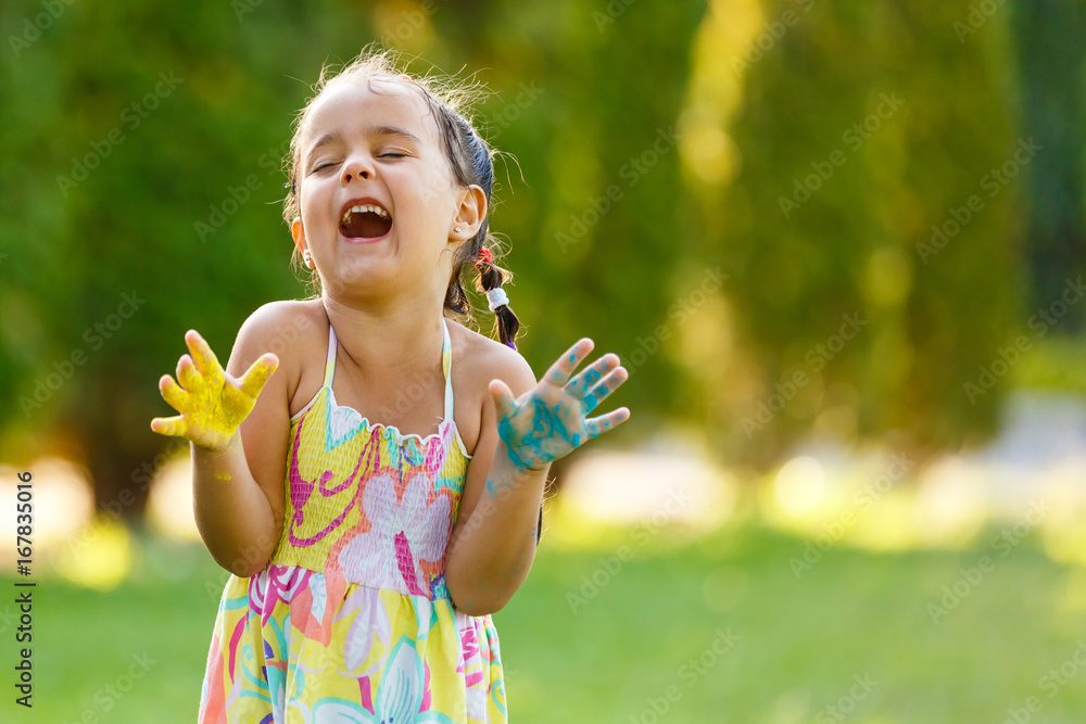 Laughing little girl showing hands in paint walking in the park Laughing little girl showing hands in paint walking in the park