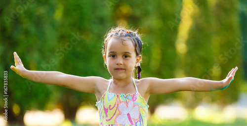 Happy little girl with her hands up on the green wheat field