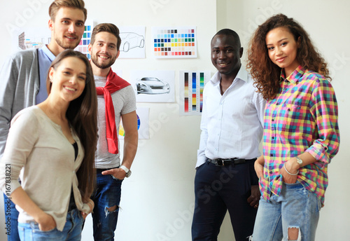 Collaboration is a key to best results. Group of young modern people in smart casual wear planning business strategy while young man pointing at infographic displayed on white wall in the office photo