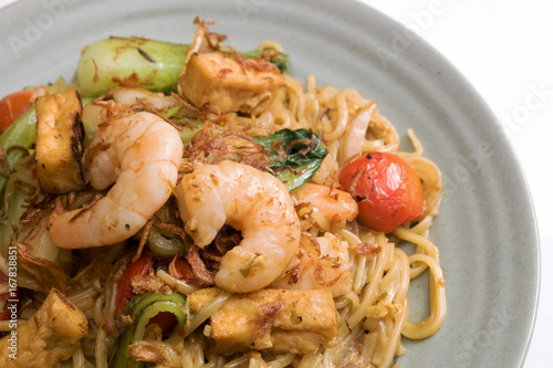 
Mie goreng, fried yellow noodle. with prawn seafood vegetable tomato choy egg garlic shallot onion shrimp cabbage on gray plate white table cloth. Deliciously famous indonesian Malaysian spicy dish. photo