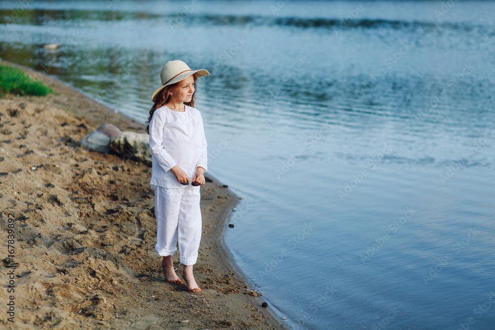 Portrait of a cute little girl in a white dress standing on the river bank Portrait of a cute little girl in a white dress standing on the river bank