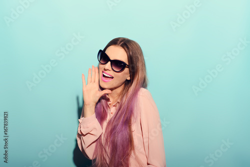 Surprised beautiful young woman in pink shirt posing with hand on chin and looking away. Three quarter length studio shot on turquoise background.