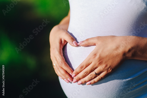 A woman's hands being held in the shape of a heart over her pregnant belly. Parenthood and happiness concept.