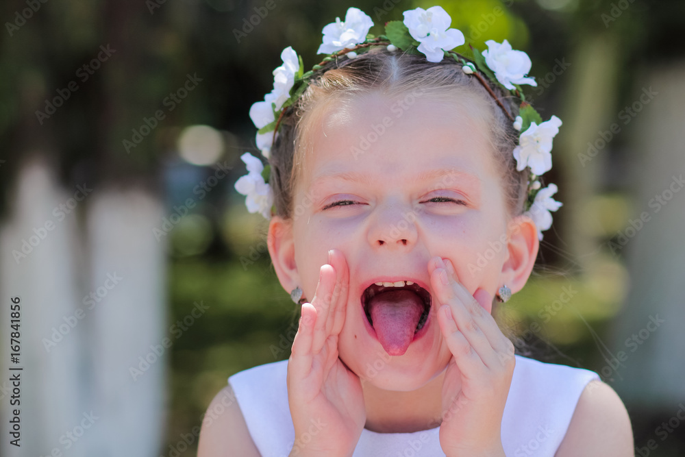 little girl showing tongue and covers his face with his hands, a child with a wreath of