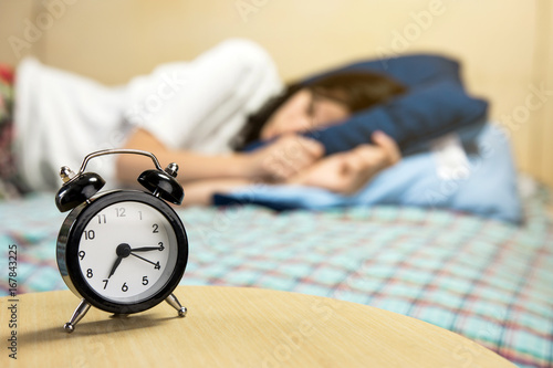 Black Alarm Clock With Blurred Sleeping Young Woman At The Background