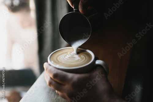 person making latte art in white cup on dark wood table