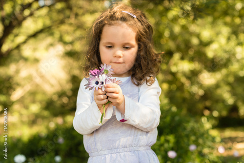 Half length view of little girl holding bouquet of purple and white diaisies  selective focus 