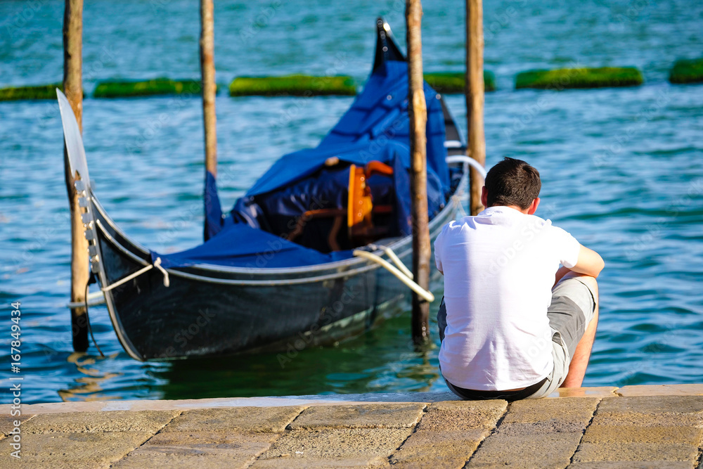 Venice, Italy - July, 28, 2017: man sits near the gondola in Venice, Italy