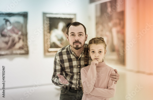 cheerful father and daughter regarding paintings in museum