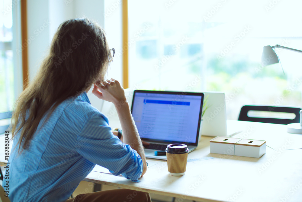 Young woman sitting in office table, looking at laptop computer screen . Young woman Young woman sitting in office table, looking at laptop computer screen . Young woman