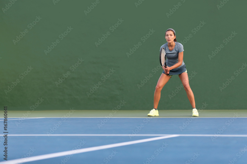 Tennis player woman standing ready to play waiting to receive serve. Outdoor fitness instructor focused playing on hard court on green background.