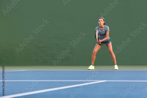 Tennis player woman standing ready to play waiting to receive serve. Outdoor fitness instructor focused playing on hard court on green background.