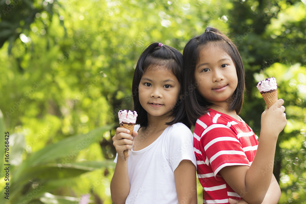 Two girls holding strawberry ice cream cone and looking for camera in the garden. Makes you feel refreshed, relaxed and happy time. (Dear friend concept) Two girls holding strawberry ice cream cone and looking for camera in the garden. Makes you feel refreshed, relaxed and happy time. (Dear friend concept)