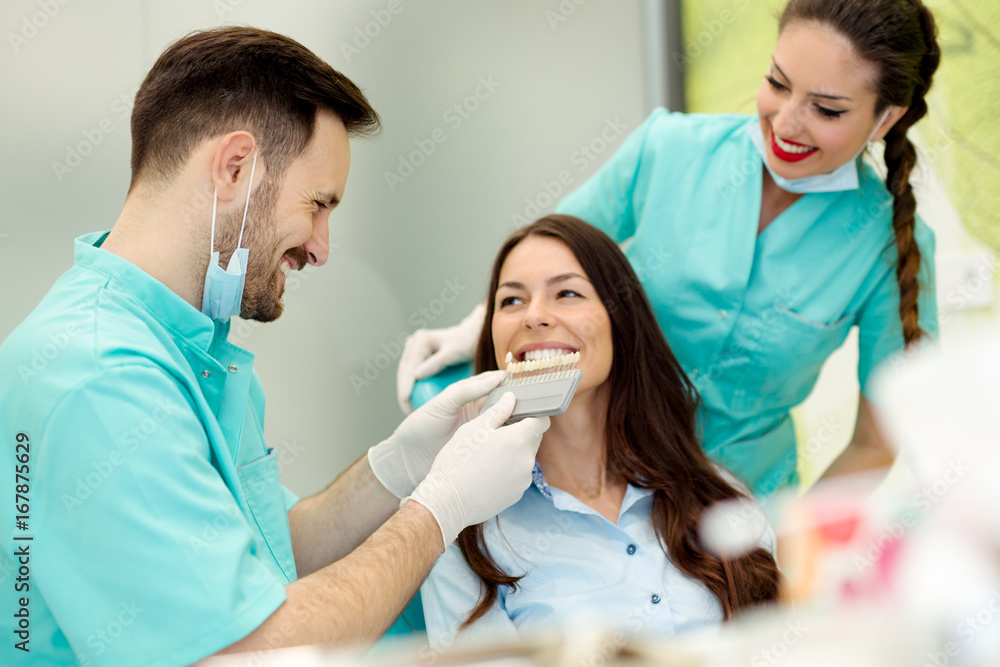 Dentist checking and selecting color of young woman's teeth Dentist checking and selecting color of young woman's teeth
