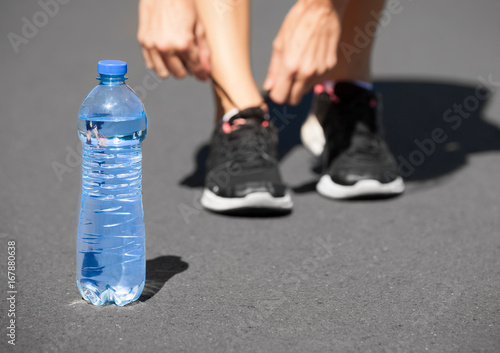 Drinking water , and fitness concept. Runner tying shoelace next to bottle of water. 