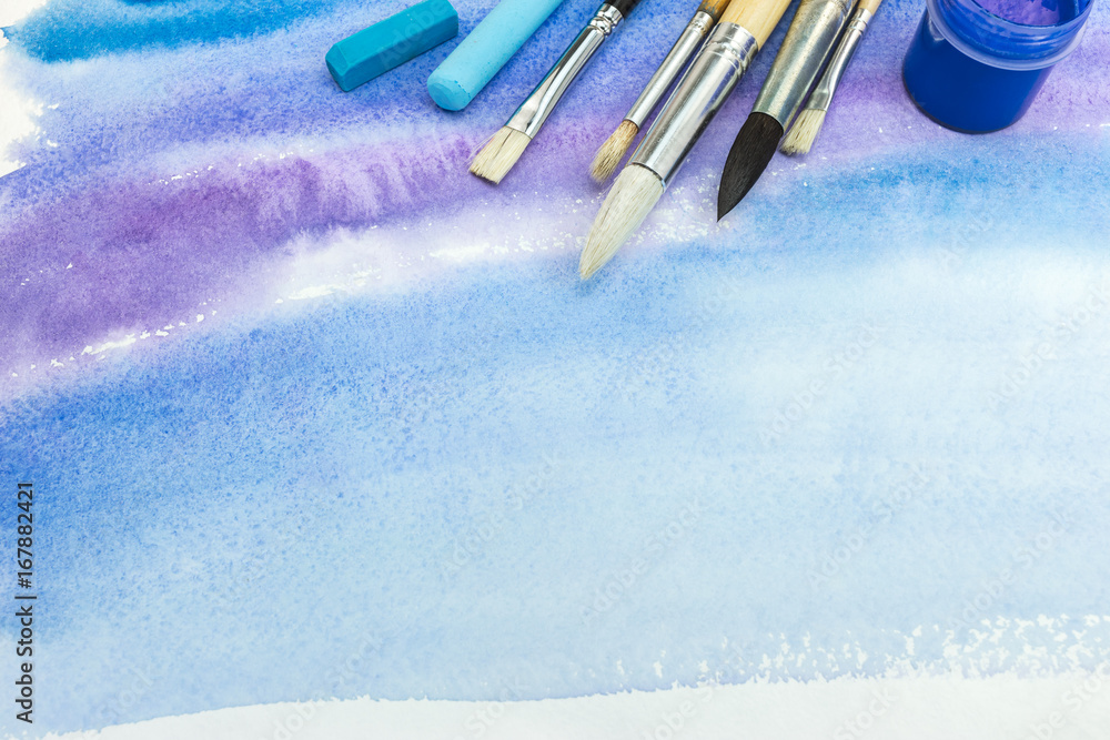 Fototapeta premium set of paintbrushes and paints with pastel crayons on blue watercolor background