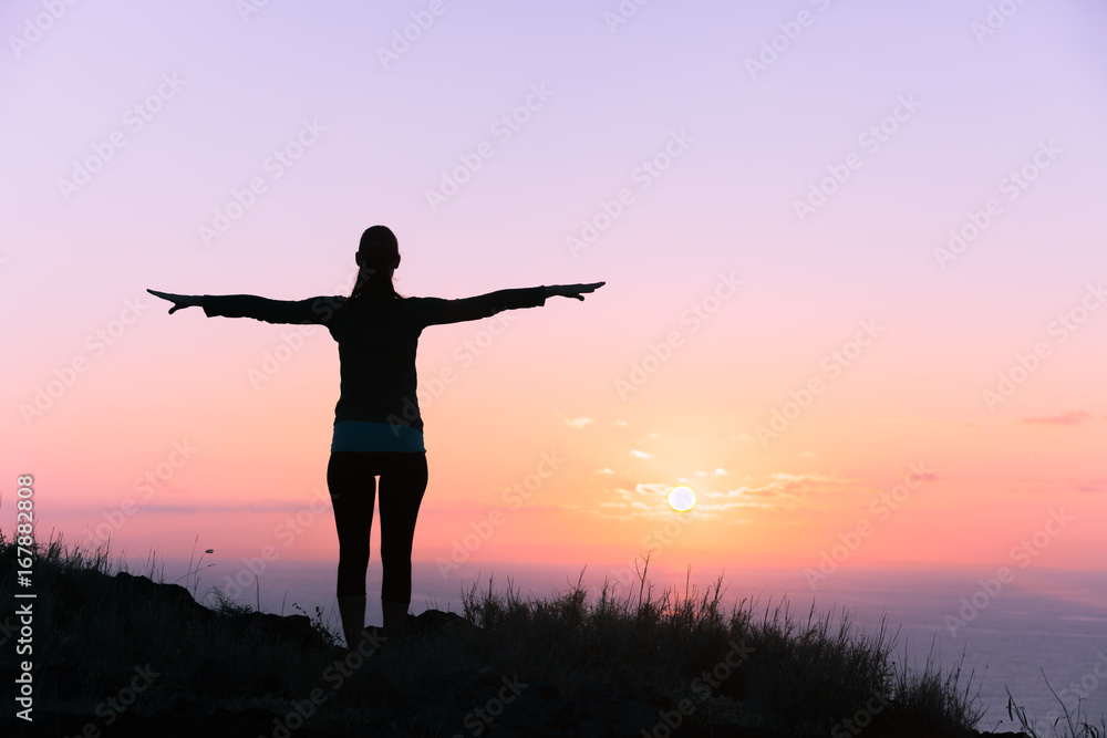 Freedom, new day concept. Back light silhouette of woman with her arms stretched, over looking a beautiful ocean sunset. 
