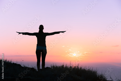 Freedom, new day concept. Back light silhouette of woman with her arms stretched, over looking a beautiful ocean sunset. 