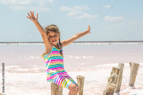 Little girl on the background of salt lakes of the dead sea and pink rose, raised her hands up