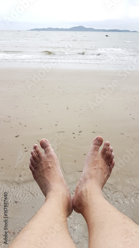 Relax of man feet above the wet beach point to the sea