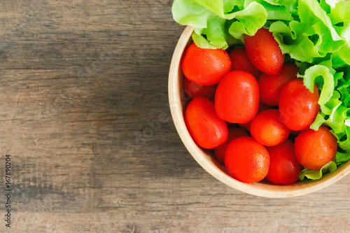 Fresh tomato and lettuce in wood bowl put on wood table. Top view or flat lay of tomato and green oak lettuce with copy space for background. Fresh green oak lettuce and tomato prepare for cooking.