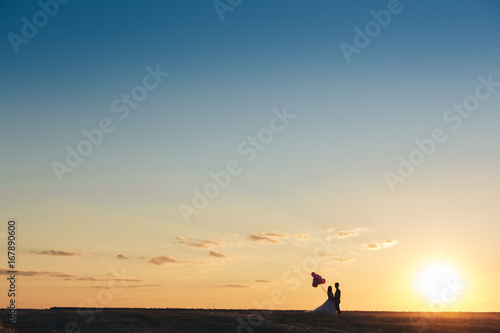 Bride and groom in a field at sunset with balloon