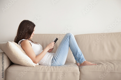 Young woman enjoying bestseller book sitting on couch during free time, teenage student studying textbook before exam, lonely introvert girl spending time at home with literature, reading as hobby