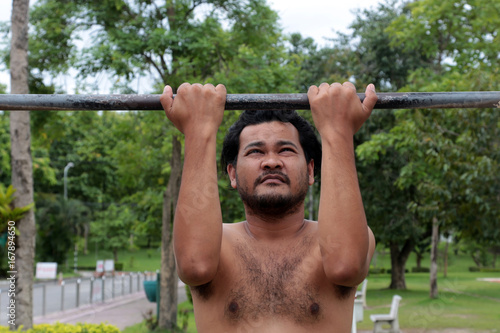 Asian man doing pull-ups on a horizontal bar in the park for healthy.