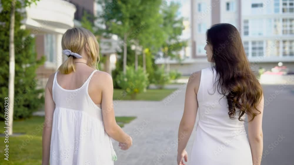Two amazing women wearing white dresses are walking down an alley and peacfully talking about something Two amazing women wearing white dresses are walking down an alley and peacfully talking about something