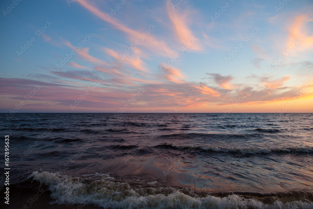 North seascape on Lake Onega - waves beat against the granite shore which reflects the rays of the setting sun.