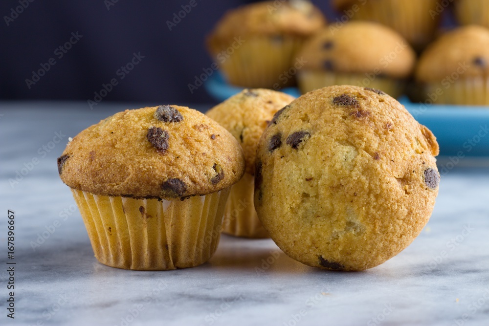 Miniature vanilla chocolate chips muffins on marble surface in front of blue plate with some more muffins