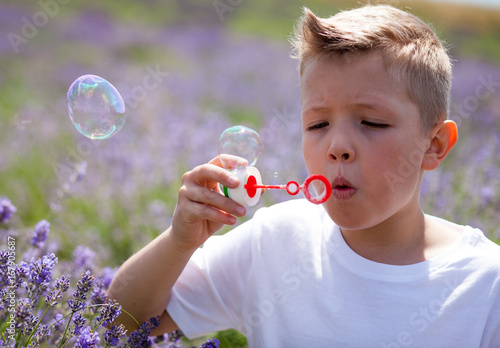 Cute boy blowing soap bubbles and having fun in lavender field