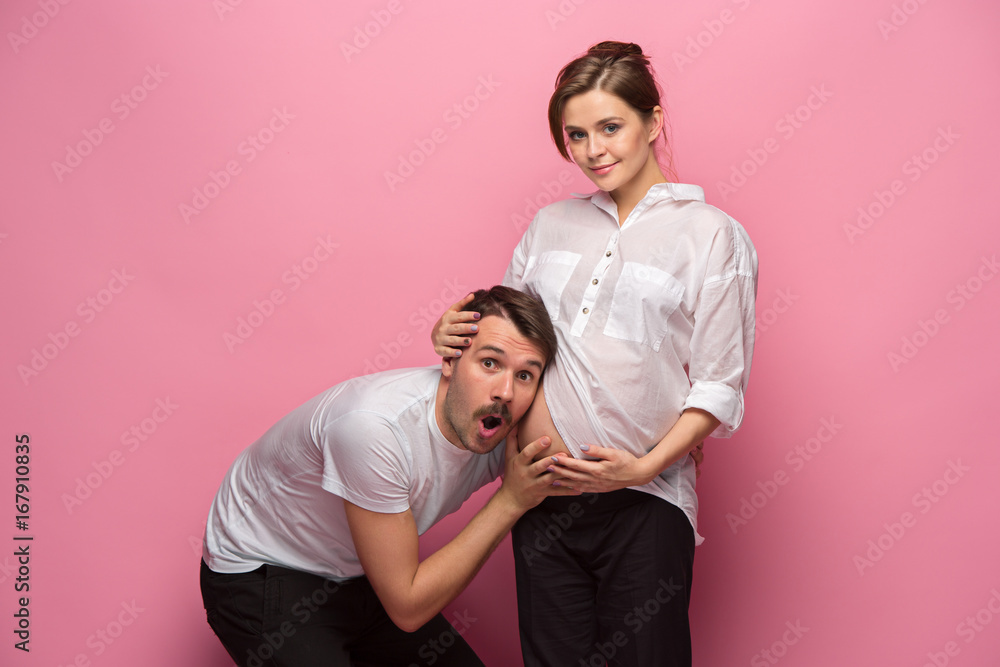 Obraz premium Handsome man is listening to his beautiful pregnant wife's tummy and smiling