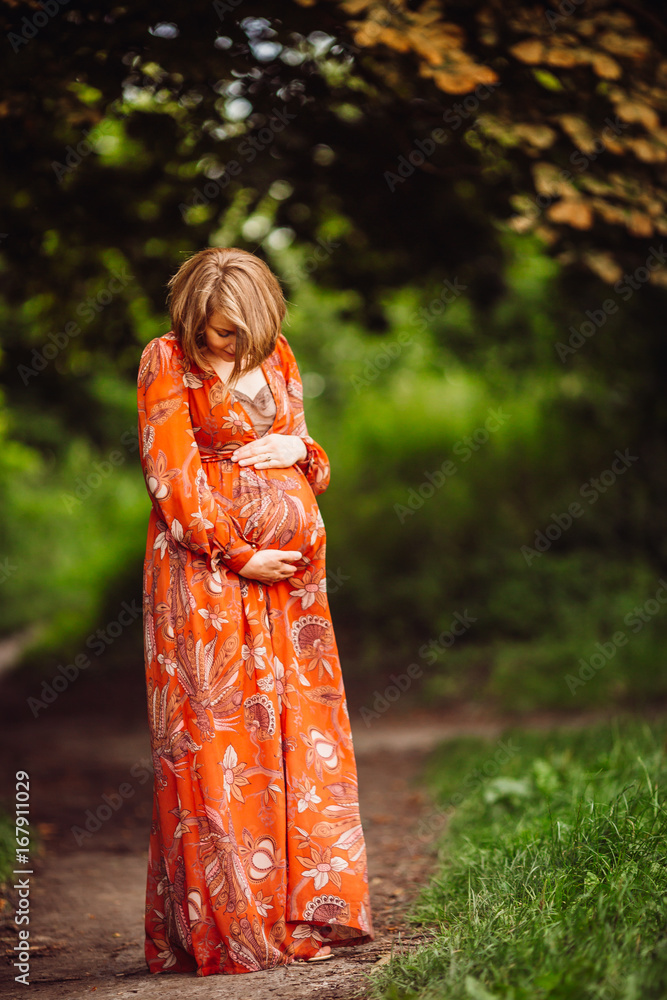 Beautiful pregnant woman in orange dress poses in the forest