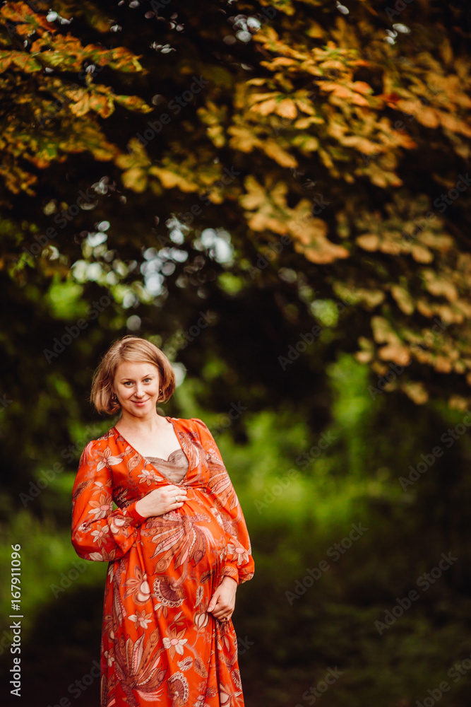 Beautiful pregnant woman in orange dress poses in the forest Beautiful pregnant woman in orange dress poses in the forest