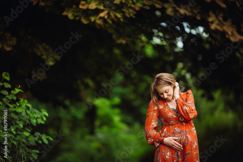Beautiful pregnant woman in orange dress poses in the forest