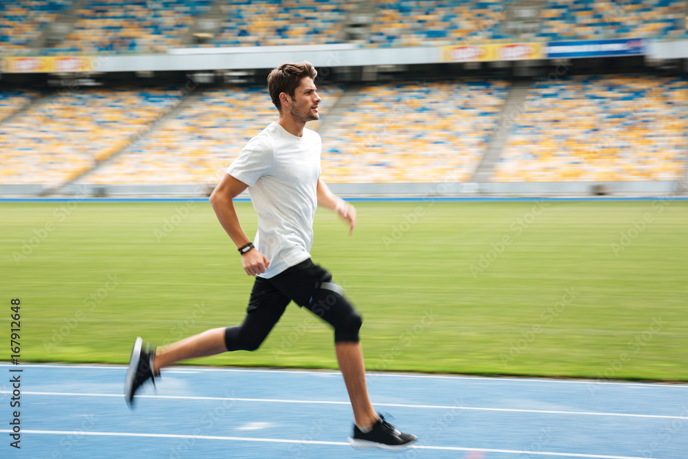 Side view of a young sportsman running on a racetrack