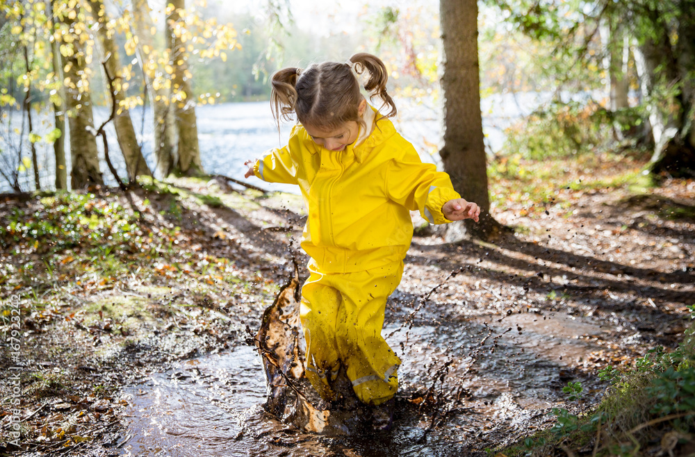 Cute little girl jumping in muddy puddle wearing yellow rubber overalls.  Happy childhood. Sunny autumn forest Stock Photo | Adobe Stock