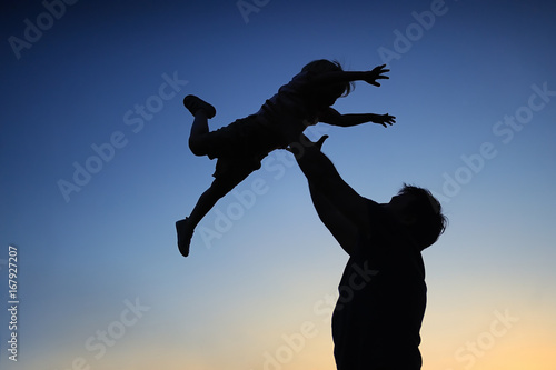 Loving father and his little son having fan together outdoors. Family as silhouette on sunset.