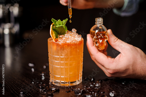 small skull-shaped bottle, orange cocktail and barmen hand photo