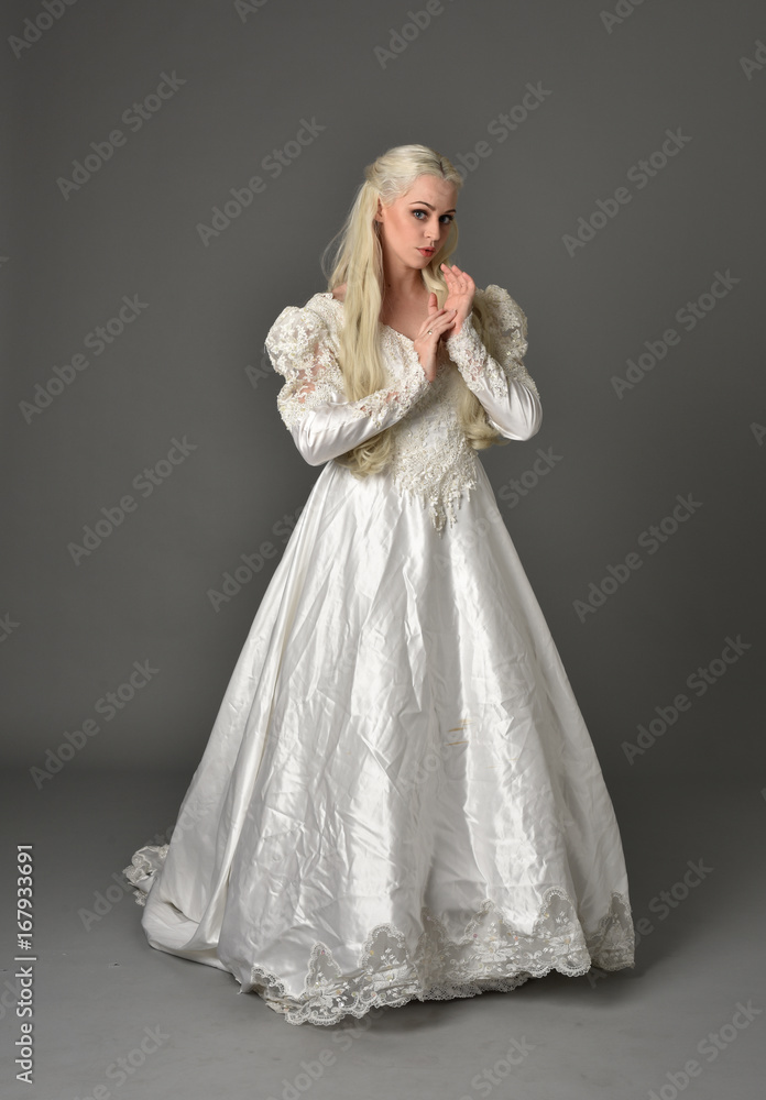 full length portrait of a beautiful blonde woman wearing link white gown, standing pose against a grey background. full length portrait of a beautiful blonde woman wearing link white gown, standing pose against a grey background.