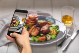 Photographing food concept - woman takes picture of hot meat dishes. Pork ribs grilled with salad and apples on a plate.